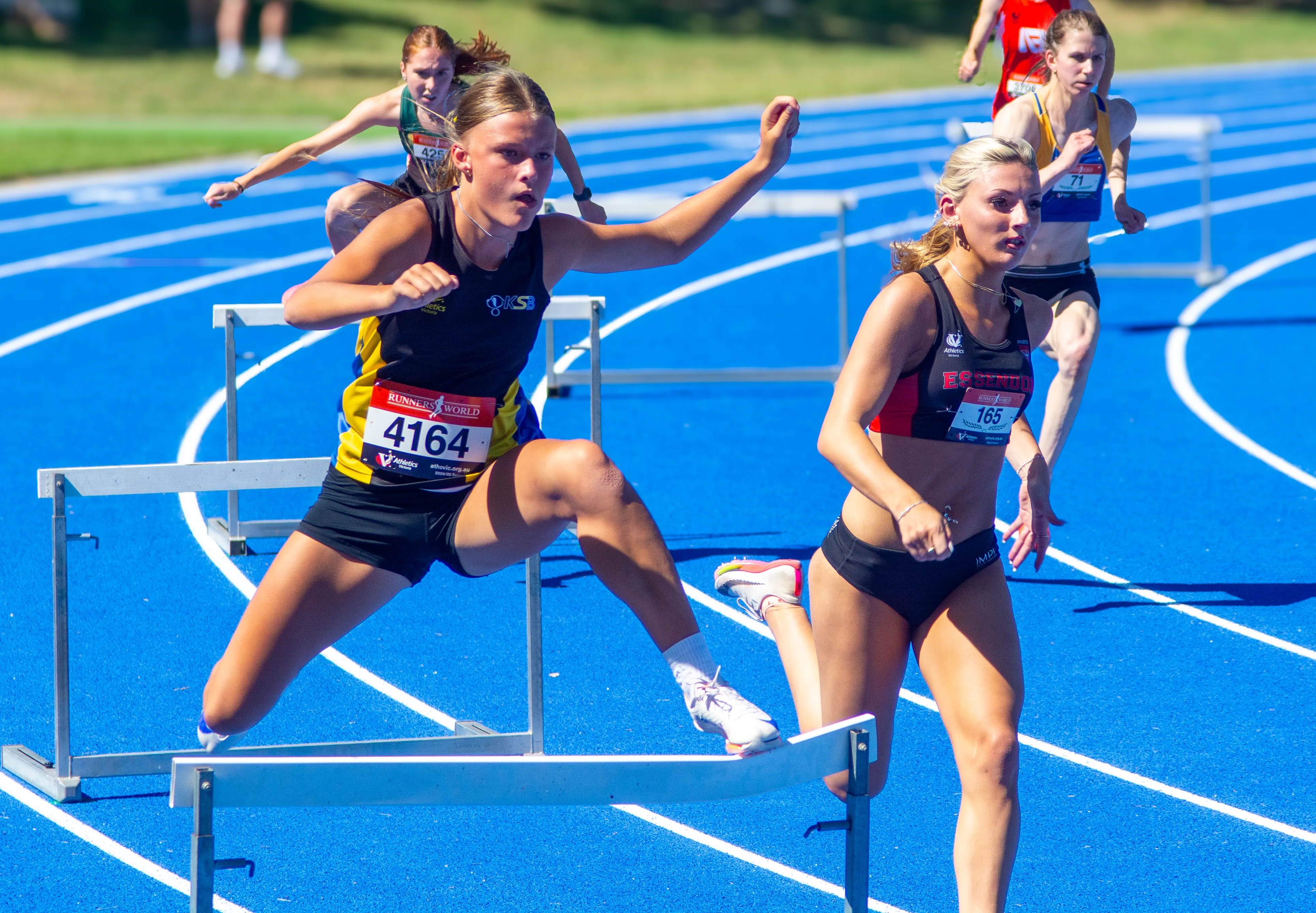 An athlete clears a hurdle mid-race, captured with professional sports photography.